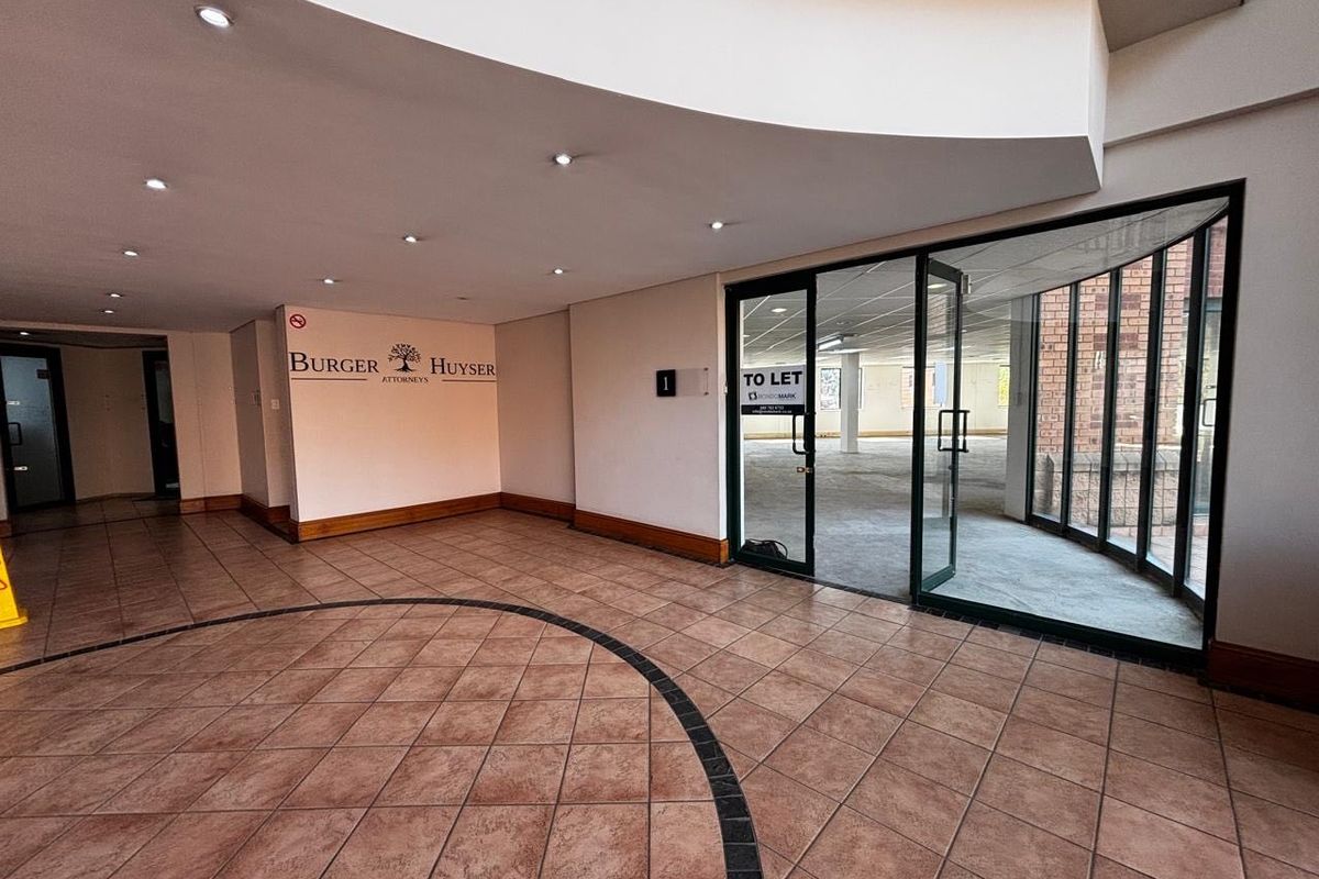 Spacious commercial entrance lobby featuring tiled flooring, recessed downlighting, and a modern curved ceiling bulkhead leading into an open-plan office space.