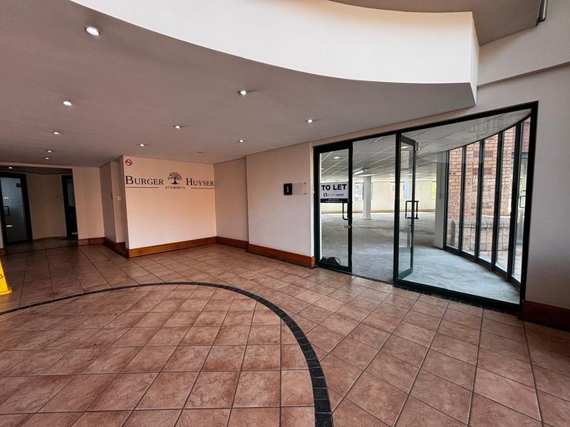 Spacious commercial entrance lobby featuring tiled flooring, recessed downlighting, and a modern curved ceiling bulkhead leading into an open-plan office space.