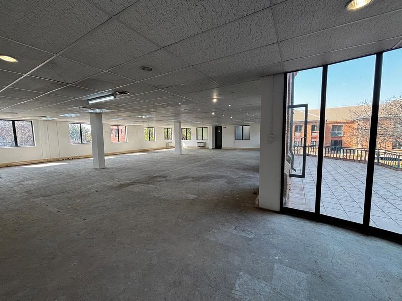 Spacious open-plan commercial office area featuring a suspended ceiling, structural columns, and direct access to an outdoor tiled balcony.