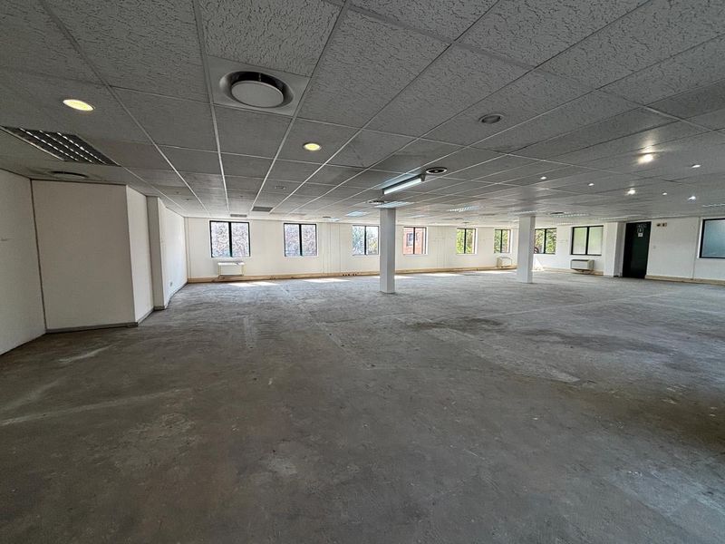 A large, open-plan commercial office space featuring a suspended ceiling, recessed lighting, structural columns, and expansive windows, currently awaiting floor finishing.
