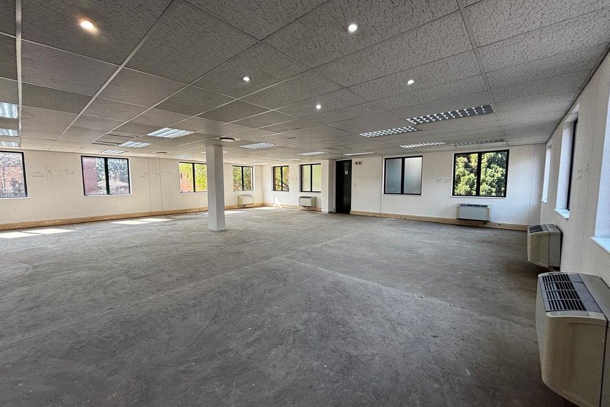 Spacious open-plan commercial office area featuring a suspended ceiling, recessed lighting, multiple air conditioning units, and large windows providing ample natural light.