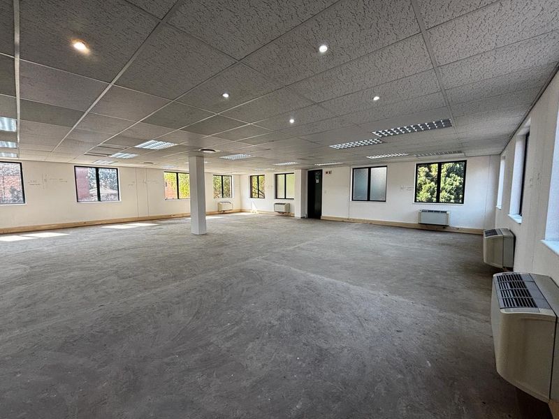 Spacious open-plan commercial office area featuring a suspended ceiling, recessed lighting, multiple air conditioning units, and large windows providing ample natural light.