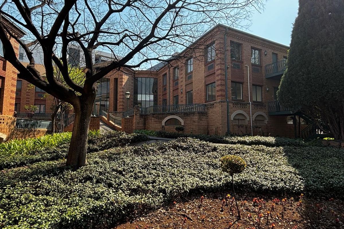 A well-maintained commercial building exterior featuring classic brick architecture, landscaped garden areas, and accessible outdoor walkways.