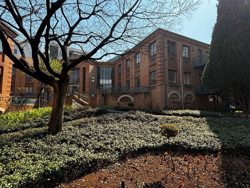 A well-maintained commercial building exterior featuring classic brick architecture, landscaped garden areas, and accessible outdoor walkways.