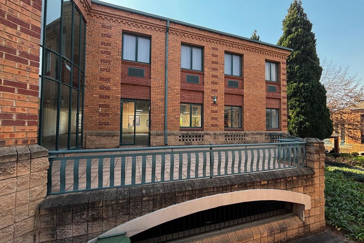 A commercial building exterior featuring a brick facade, large glass curtain wall, and a paved terrace area with metal railings.