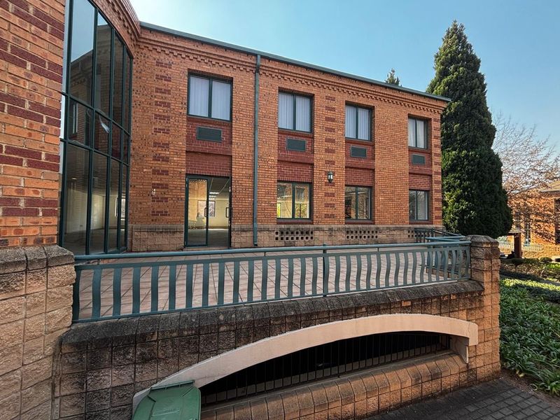 A commercial building exterior featuring a brick facade, large glass curtain wall, and a paved terrace area with metal railings.