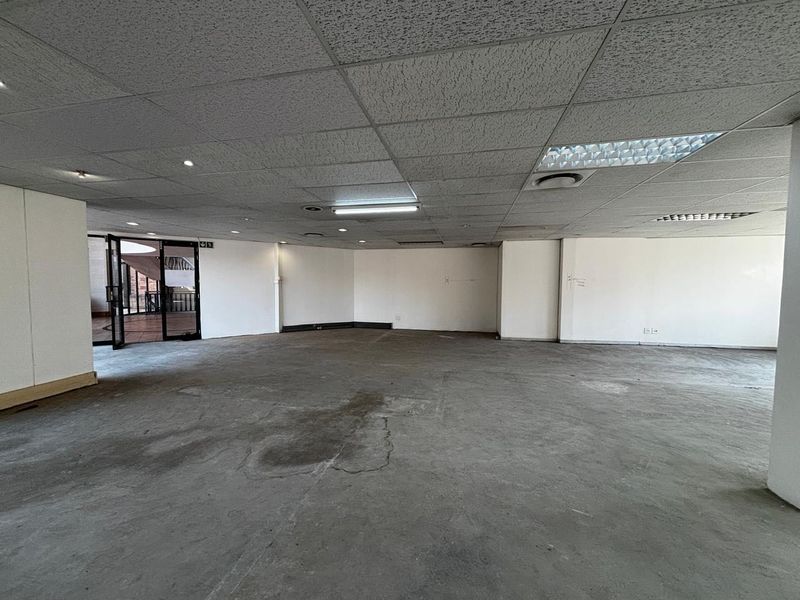 An empty commercial office space featuring a suspended ceiling, recessed lighting, and exposed concrete flooring, ready for tenant customization.