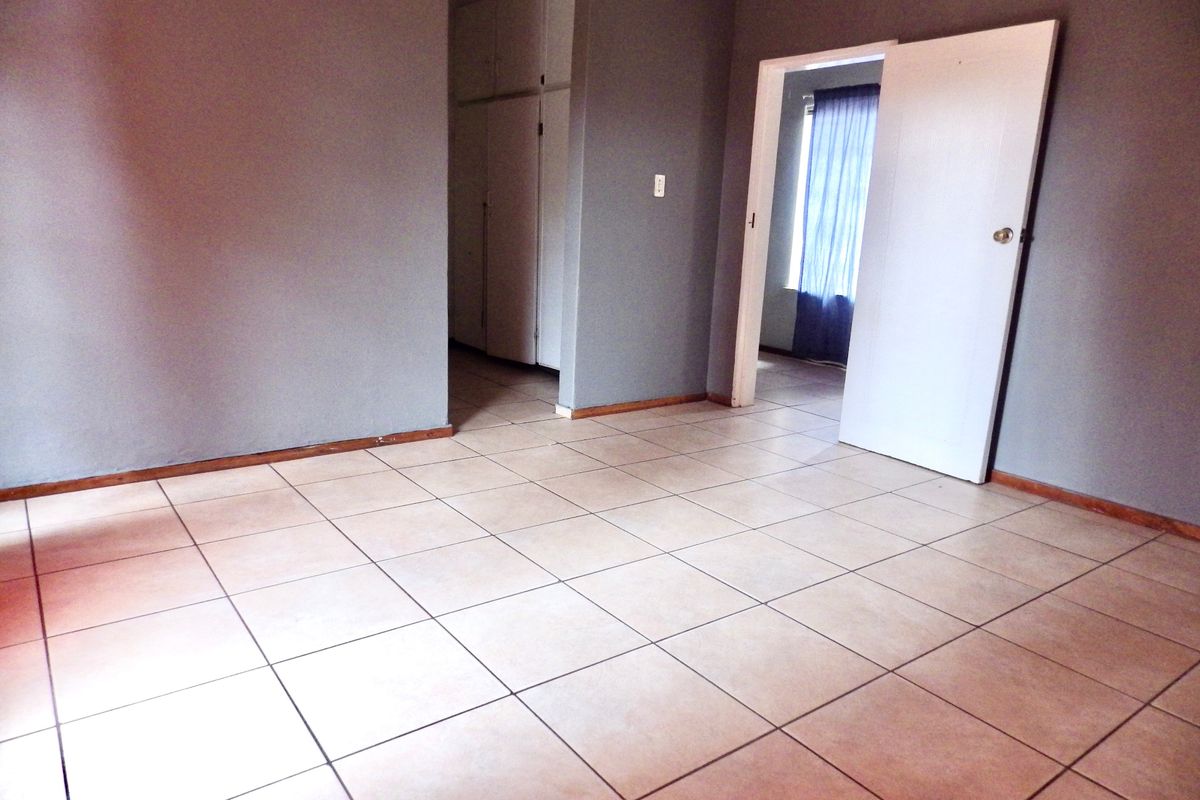 An empty bedroom featuring neutral tiled flooring, built-in cupboards, and direct access to an adjoining room.