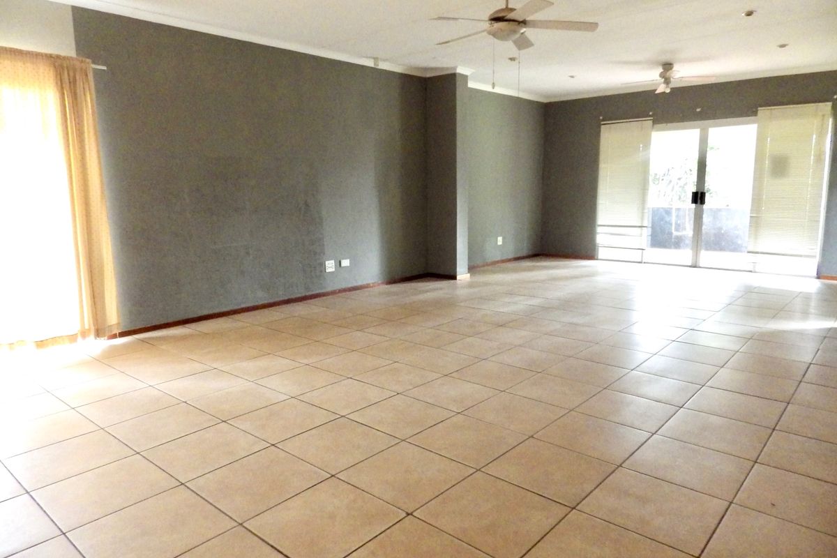Spacious, empty living area featuring neutral tiled flooring, dual ceiling fans, and sliding glass doors providing access to the exterior.