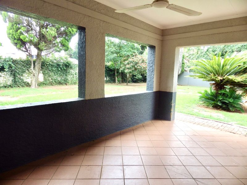 A covered outdoor patio featuring tiled flooring, a ceiling fan, and open views overlooking the garden area.