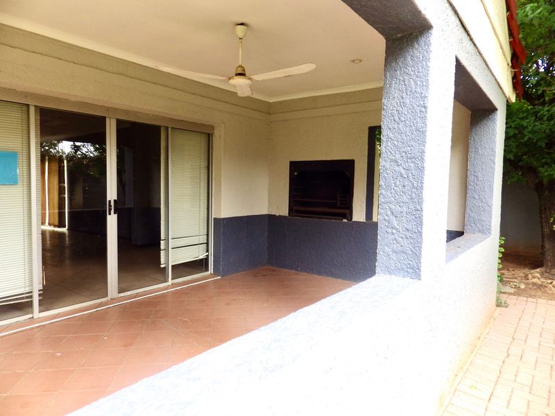 Covered patio area featuring a built-in braai, ceiling fan, and sliding glass doors leading into the home.