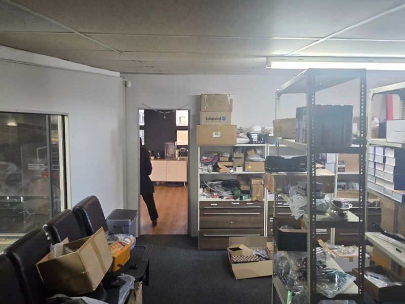 Industrial utility or storage space featuring a suspended ceiling, fluorescent lighting, and an internal glass partition, currently utilized for inventory storage.