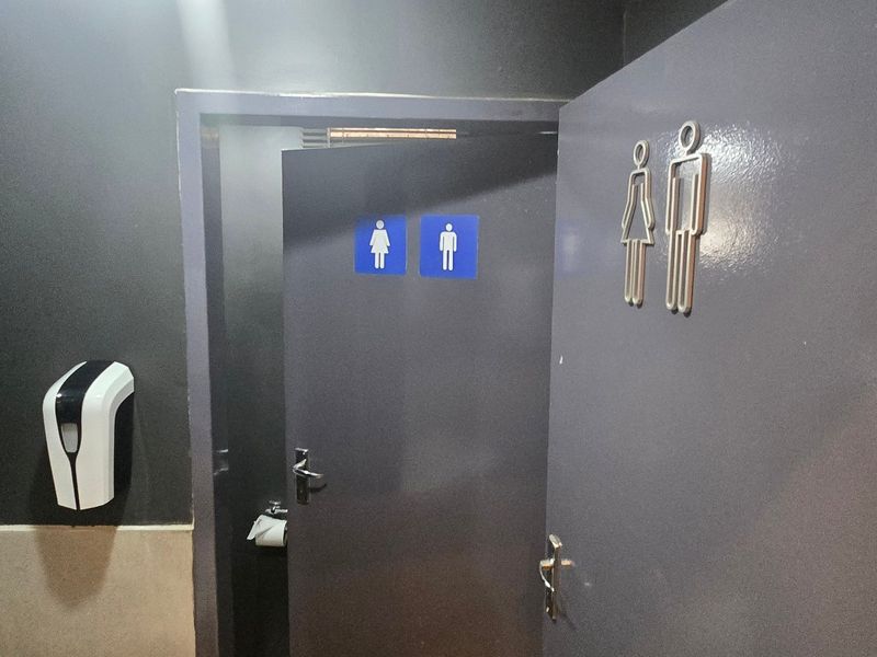 A functional industrial restroom facility featuring clear signage, wall-mounted soap dispenser, and a framed mirror.