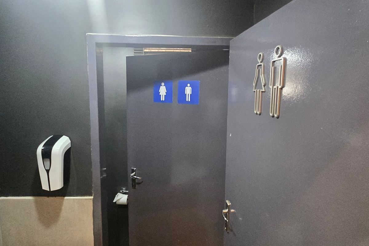 A functional industrial restroom facility featuring clear signage, wall-mounted soap dispenser, and a framed mirror.