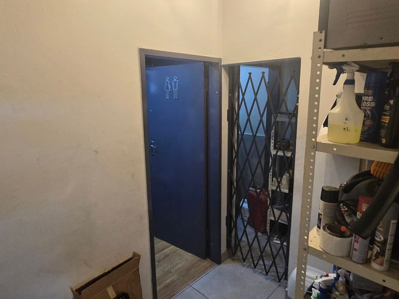 A functional hallway area featuring tiled flooring, a security gate, and access to restroom facilities within an industrial property setting.