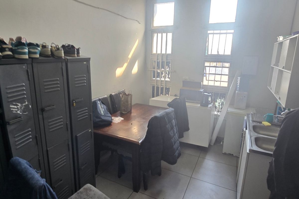 A functional industrial kitchen area featuring tiled flooring, double sink, and security-barred windows, providing a practical space for staff or utility use.