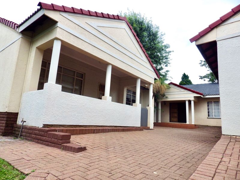 Front view of the property featuring a paved driveway, covered patio area with columns, and a tiled roof structure.