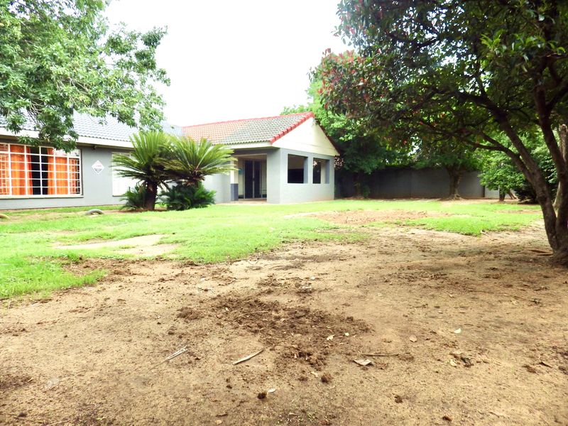 A view of the rear garden featuring a covered patio, tiled roof, and established trees with a mix of lawn and exposed soil areas.