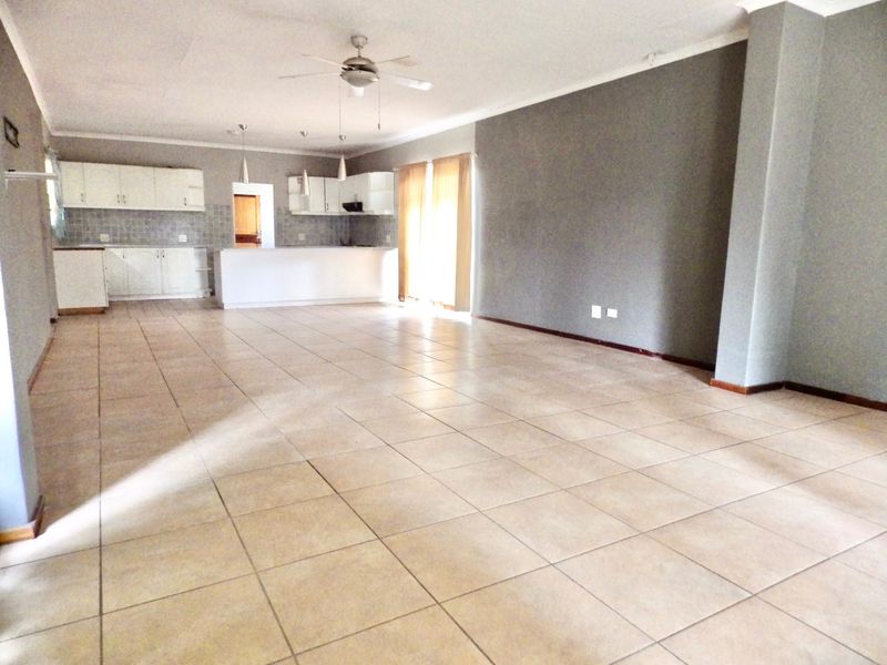 Spacious open-plan living area featuring tiled flooring, a ceiling fan, and a functional kitchen with built-in cabinetry and a central island.