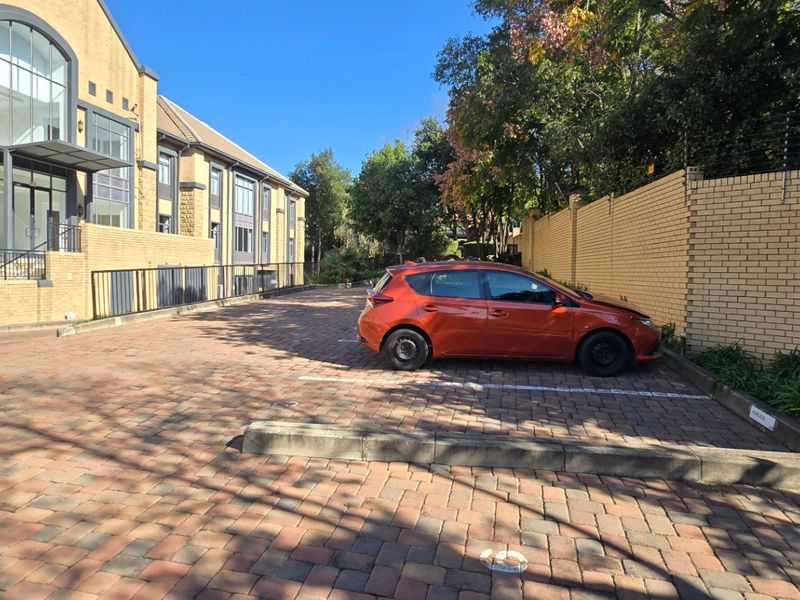 Exterior view of a commercial property featuring a paved parking area, facebrick building facade, and secure perimeter wall with electric fencing.