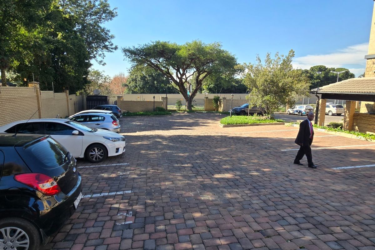 A paved commercial parking area featuring a brick boundary wall and a covered entrance section, providing ample space for vehicles.