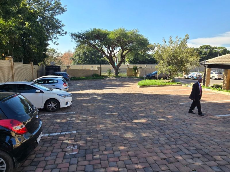 A paved commercial parking area featuring a brick boundary wall and a covered entrance section, providing ample space for vehicles.