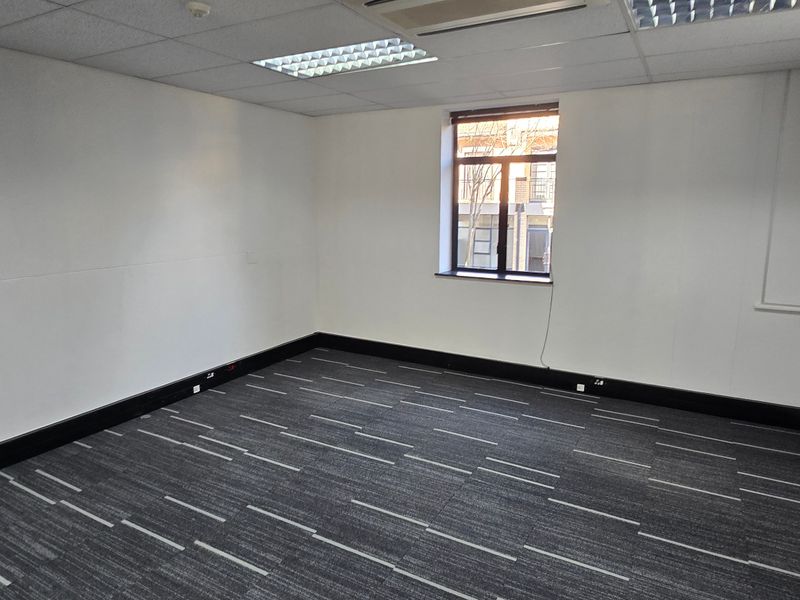 A clean, empty commercial office space featuring neutral walls, carpet tile flooring, and recessed ceiling lighting.