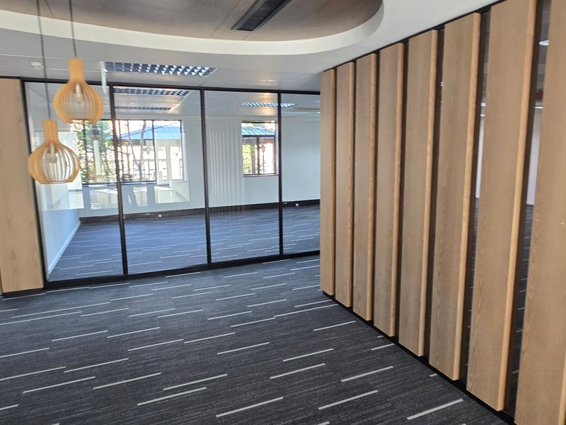 Modern commercial office space featuring glass partitions, a timber slat feature wall, recessed ceiling details, and high-quality carpet tiles.