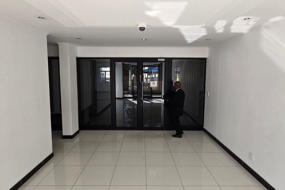 A bright, modern commercial entrance area featuring neutral tiled flooring, recessed lighting, and large glass-panelled doors providing clear visibility and access.