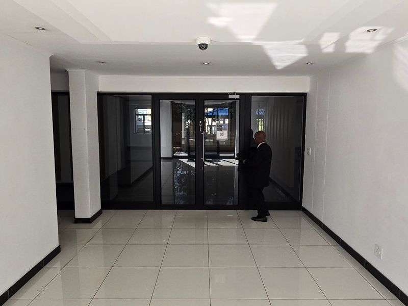 A bright, modern commercial entrance area featuring neutral tiled flooring, recessed lighting, and large glass-panelled doors providing clear visibility and access.