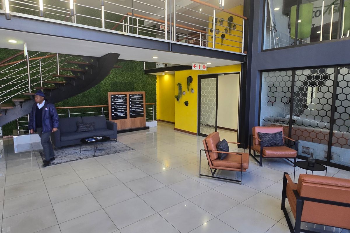 Modern commercial entrance lobby featuring a double-volume ceiling, floating staircase, mezzanine level, and contemporary glass partitioning with tiled flooring throughout.