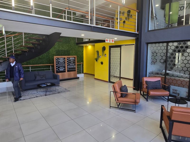 Modern commercial entrance lobby featuring a double-volume ceiling, floating staircase, mezzanine level, and contemporary glass partitioning with tiled flooring throughout.