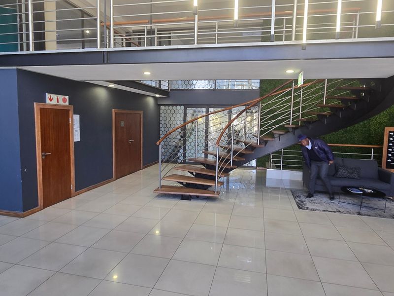 Modern commercial building entrance featuring a striking floating staircase, mezzanine level, tiled flooring, and a decorative artificial green wall.