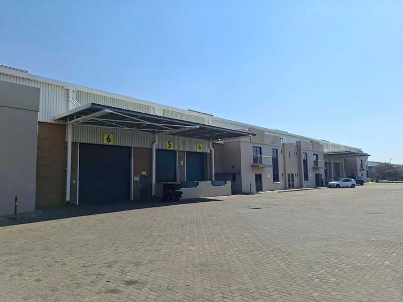 Industrial warehouse exterior featuring multiple loading bays with roller shutter doors, a metal canopy, and a spacious paved yard area.