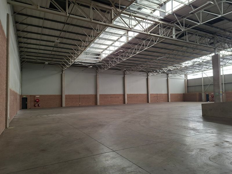 Spacious industrial warehouse unit featuring high ceilings with exposed steel trusses, abundant natural light from skylights, and durable concrete flooring.