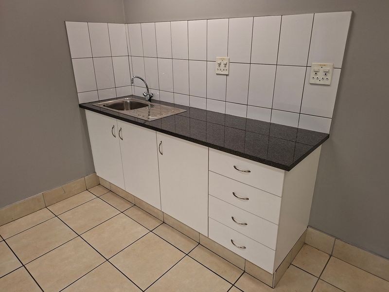 A clean and functional scullery or kitchenette area featuring a stainless steel sink, granite countertop, and white built-in cabinetry with tiled backsplash.