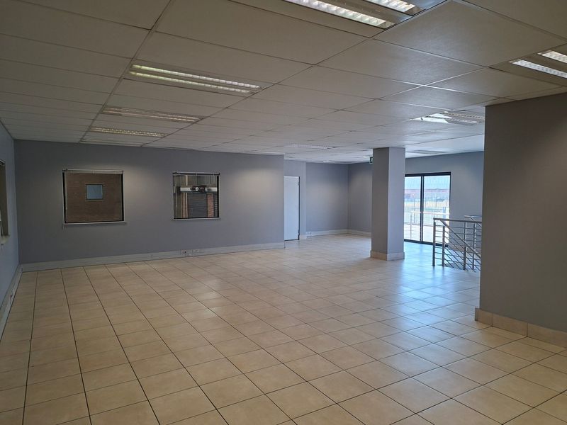 Spacious, open-plan office area featuring neutral grey walls, ceramic tile flooring, and a suspended ceiling with recessed lighting.