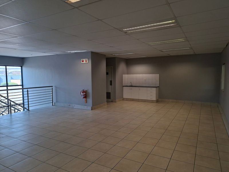 Spacious open-plan industrial office area featuring tiled flooring, a suspended ceiling with recessed lighting, and a functional kitchenette corner.