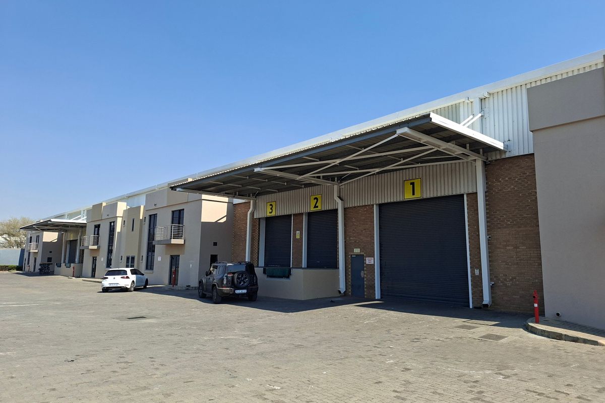 Industrial warehouse exterior featuring multiple roller shutter doors, loading bays with metal canopies, and a spacious paved yard area.