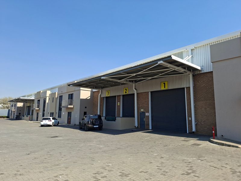 Industrial warehouse exterior featuring multiple roller shutter doors, loading bays with metal canopies, and a spacious paved yard area.