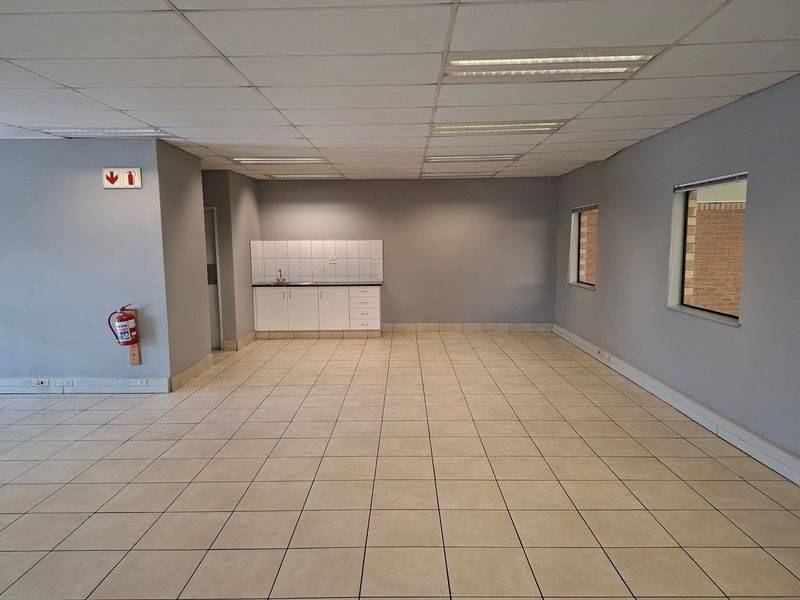 An open-plan industrial utility space featuring tiled flooring, a suspended ceiling with integrated lighting, and a functional kitchenette area with a sink.