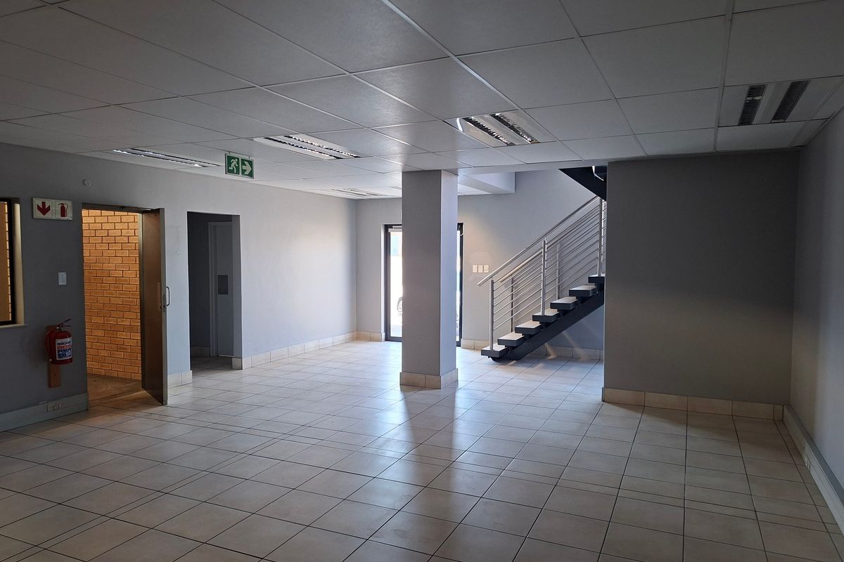 Spacious industrial entry area featuring ceramic tiled flooring, a modern staircase with metal balustrades, suspended ceilings, and neutral grey wall finishes.