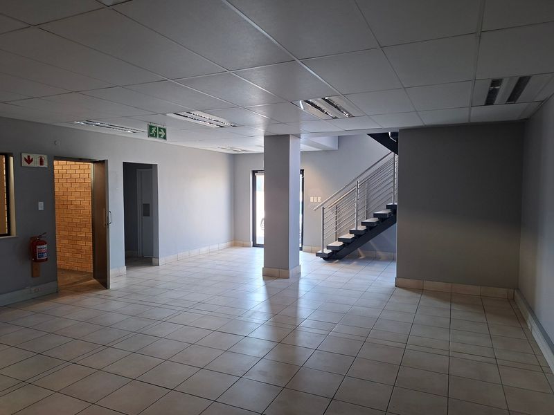 Spacious industrial entry area featuring ceramic tiled flooring, a modern staircase with metal balustrades, suspended ceilings, and neutral grey wall finishes.