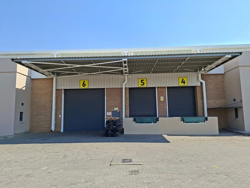 Industrial warehouse exterior featuring three loading bays with roller shutter doors, dock levelers, and a protective steel canopy over a paved yard.