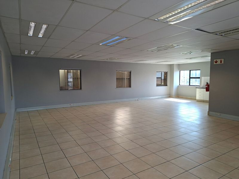 Spacious open-plan office area featuring neutral ceramic floor tiles, a suspended ceiling with recessed lighting, and built-in storage cabinetry.