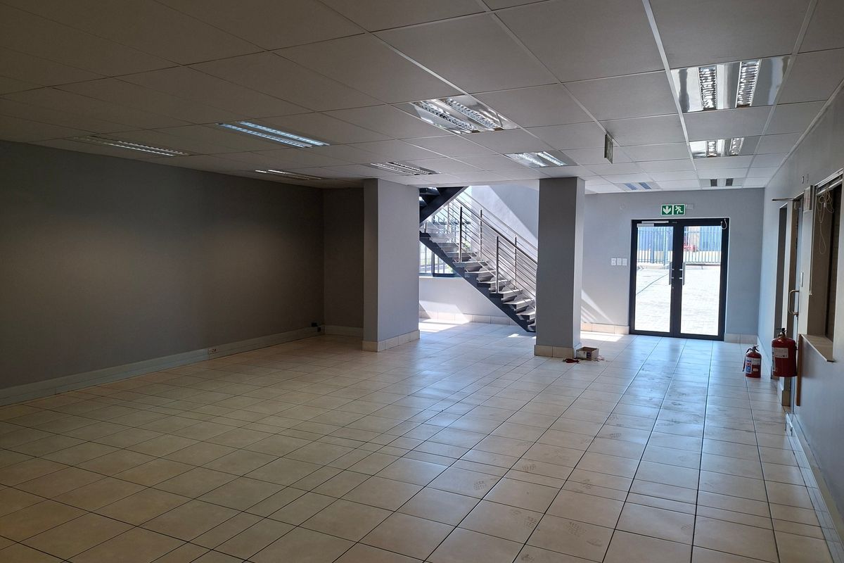 Spacious open-plan industrial office area featuring ceramic tiled flooring, a suspended ceiling with recessed lighting, and an internal metal staircase.