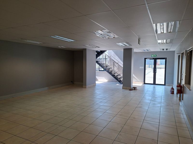 Spacious open-plan industrial office area featuring ceramic tiled flooring, a suspended ceiling with recessed lighting, and an internal metal staircase.