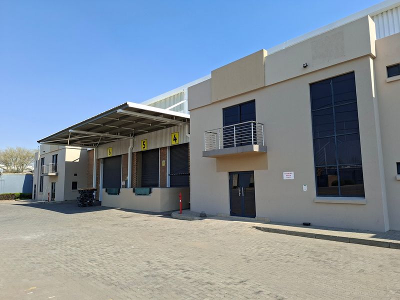 Industrial warehouse exterior featuring multiple loading bays with roller shutter doors, a paved yard, and modern architectural facade elements.