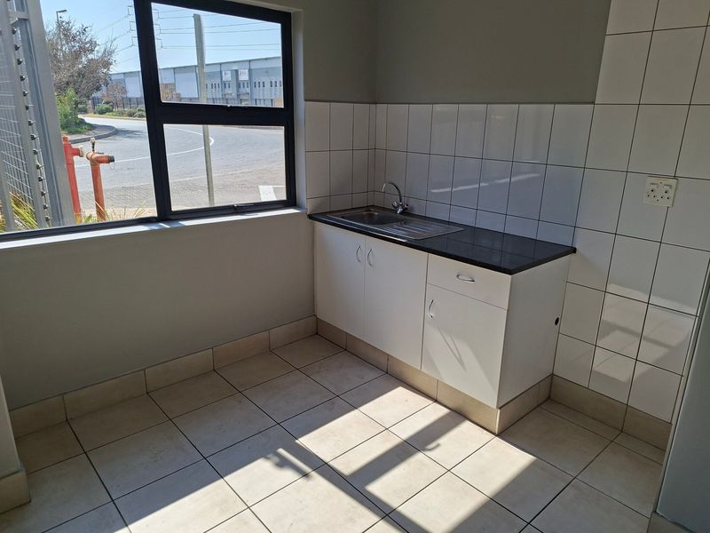 A clean, functional kitchenette area featuring a stainless steel sink, built-in cabinetry, and tiled finishes, suitable for office or industrial utility use.