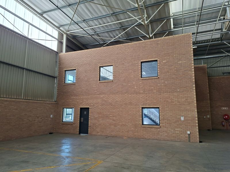 Spacious industrial warehouse interior featuring high ceilings with exposed steel trusses, concrete flooring, and a central face brick structure with internal windows.